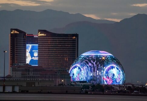 Las Vegas Sphere illuminated near hotels at dusk.