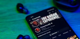 Smartphone displaying Joe Rogan Experience YouTube page earbuds nearby