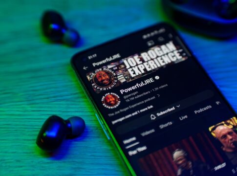 Smartphone displaying Joe Rogan Experience YouTube page earbuds nearby